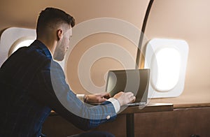 Attractive and successful businessman working on a laptop while sitting in a chair of his private jet.