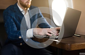 Attractive and successful businessman working on a laptop while sitting in a chair of his private jet.