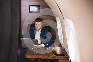 Attractive and successful businessman working on a laptop while sitting in a chair of his private jet.