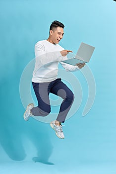 Attractive successful guy jumping in air using laptop home-based job isolated over blue background