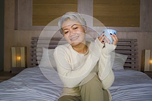 Attractive and successful mature woman with grey hair sitting on bed drinking coffee relaxed smiling happy as middle aged female