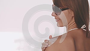 Attractive sunbathing young woman applying sunscreen to her shoulder on a warm sunny morning near the sparkling sea