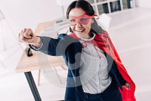 attractive super businesswoman in cape and mask standing with hand up