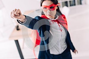 attractive super businesswoman in cape and mask standing with hand up