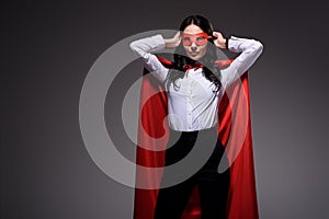 attractive super businesswoman in red cape tying mask
