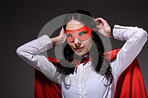 attractive super businesswoman in red cape tying mask