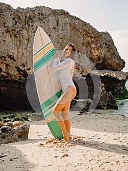 Attractive surf girl with surfboard poising at beach. Surfer woman standing at beach