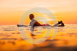 Attractive surfer woman on a surfboard in ocean. Surfgirl at sunset