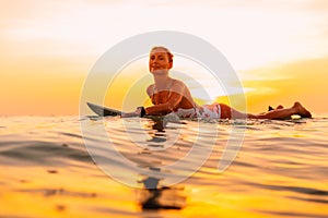 Attractive surfer woman on a surfboard in ocean. Surfgirl at sunset