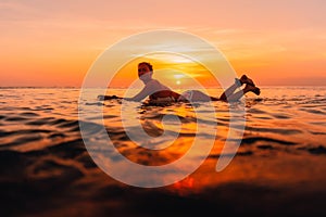 Attractive surfer woman on a surfboard in ocean. Surfgirl at sunset