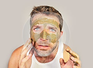 Attractive and surprised funny man horrified looking himself on bathroom mirror ugly and weird applying green cream on his face i