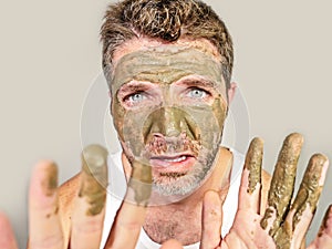 Attractive and surprised funny man horrified looking himself on bathroom mirror ugly and weird applying green cream on his face i