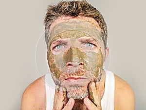 Attractive and surprised funny man horrified looking himself on bathroom mirror ugly and weird applying green cream on his face i