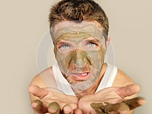 Attractive and surprised funny man horrified looking himself on bathroom mirror ugly and weird applying green cream on his face i