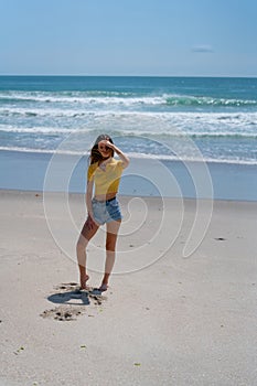 Attractive tall girl standing on beach casually with hand up shielding eyes from sun