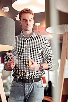 Attractive tall young mister concernedly standing in lamp store