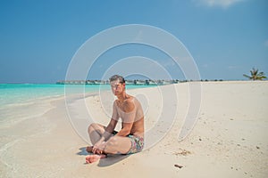 Attractive tanned man wearing swimming shorts at tropical beach at island luxury resort