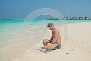 Attractive tanned sexy man wearing swimming shorts at tropical beach at island luxury resort