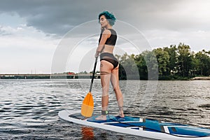 attractive tattooed woman with blue hair standup paddleboarding