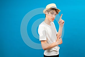 Attractive teen boy with seriosly facial expression pointing up with finger, presenting copy space