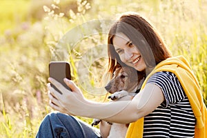 An attractive teen girl takes photos of herself and her dog using a mobile phone camera. A girl takes a photo while walking with