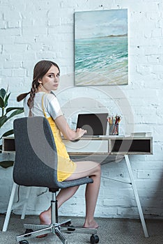 attractive teen girl using laptop and sitting at table photo