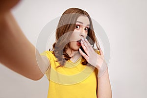 Attractive teenage girl wearing yellow casaul style T-shirt, covering mouth with palm, looking at
