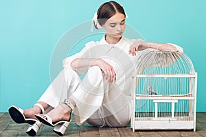 attractive teenager in white outfit with parrot in cage