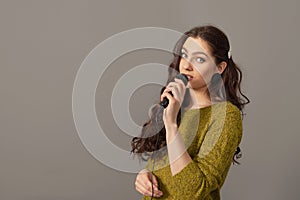 attractive teenager woman speaking with a microphone against gray background, conference speaker