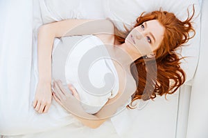 Attractive tender woman with long red hair lying in bed