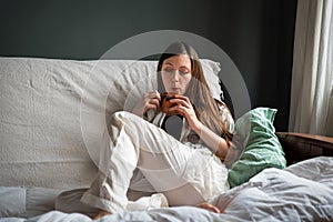 Attractive thirty year old woman in pyjama drinking coffe on her sofa in the morning