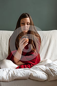 Attractive thirty year old woman in pyjama drinking coffe on her sofa in the morning