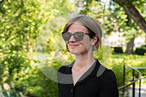 Attractive thirty year old woman with sunglasses and a black dress posing in the botanical garden during summer photo