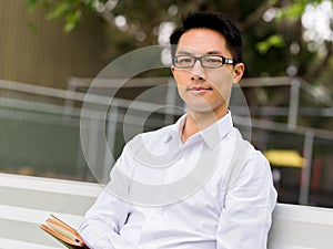 Attractive thoughtful businessman sitting on bench with notepad