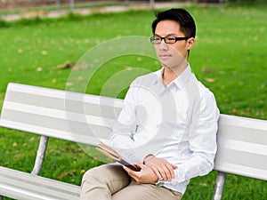 Attractive thoughtful businessman sitting on bench with notepad