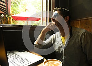 Attractive thoughtful and pensive millennial man working from internet coffee shop with laptop computer thinking relaxed as entrep