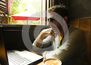 Attractive thoughtful and pensive millennial man working from internet coffee shop with laptop computer thinking relaxed as entrep