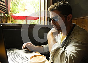 Attractive thoughtful and pensive millennial man working from internet coffee shop with laptop computer thinking relaxed as entrep