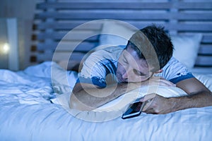 Attractive tired man in bed falling asleep while using mobile phone still holding the cellular in his hand while sleeping in inter