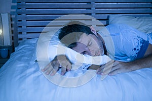 Attractive tired man in bed falling asleep while using mobile phone still holding the cellular in his hand while sleeping in inter