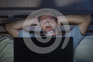 Attractive tired and stressed workaholic man working late night exhausted on bed busy with laptop computer sleepy and overworked