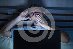 Attractive tired and stressed workaholic man working late night exhausted on bed busy with laptop computer yawning feeling sleepy