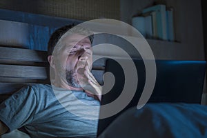 Attractive tired and stressed workaholic man working late night exhausted on bed busy with laptop computer yawning feeling sleepy