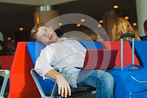 Attractive and tired traveler man with luggage taking a nap sleeping while working with laptop computer waiting for flight at