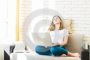 Attractive tired woman student or freelancer with laptop on her knees sitting in sofa at home. exhausted because of work