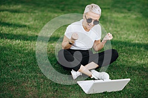 Attractive trendy happy hipster young woman with notebook in hat and sunglasses have fun in the park on the grass.