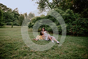 Attractive two ladies in the park enjoying the time together sitting down on the grass and chatting smiling large beside