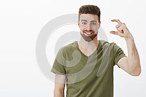 Attractive upbeat bearded sportsman in olive t-shirt shape small or tiny object telling about little effort till goal