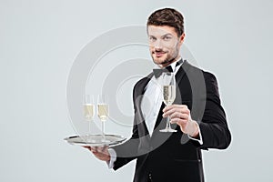 Attractive waiter in tuxedo holding tray and glass of champagne