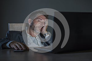 Attractive wasted and tired entrepreneur man working late night at office laptop computer desk exhausted and sleepy in financial